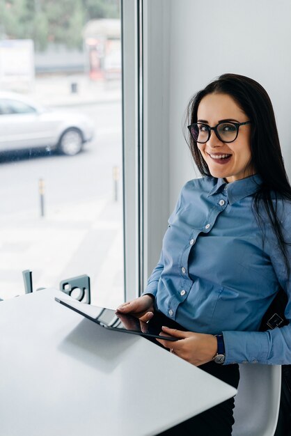 Jeune fille aux cheveux noirs drôle en chemise bleue et lunettes tenant une tablette