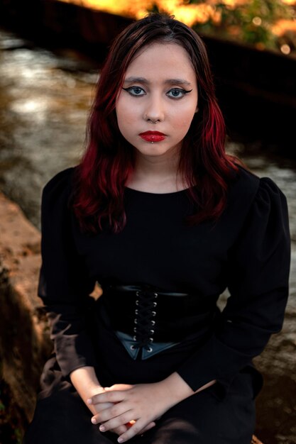 Jeune fille aux cheveux noirs de race blanche avec des stries rouges en tenue de robe noire avec ceinture corset posant pour une séance de beauté féminine