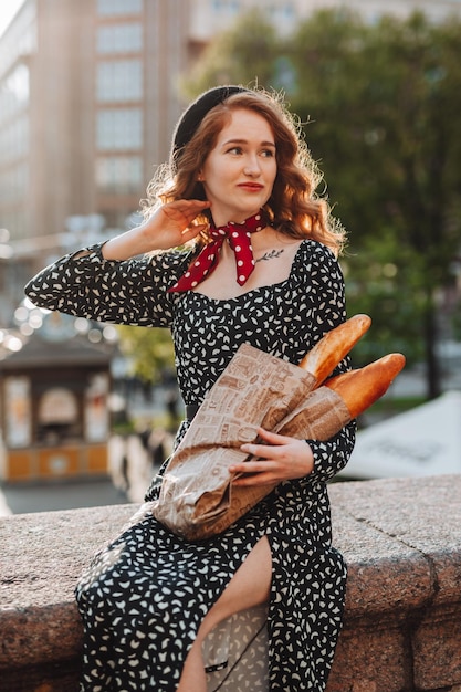 Photo une jeune fille aux cheveux rouges dans une robe noire et un béret rouge dans le contexte de la ville