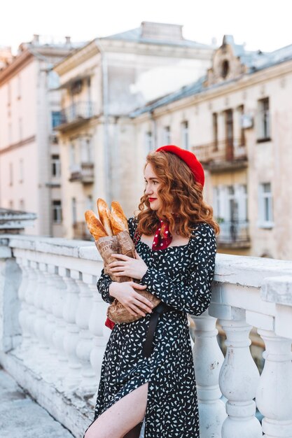 Photo une jeune fille aux cheveux rouges dans une robe noire et un béret rouge dans le contexte de la ville