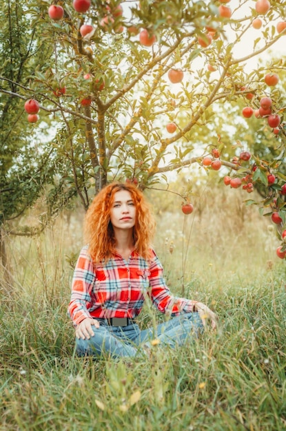 Jeune fille aux cheveux rouges est assise sous un pommier sur l'herbe verte automne air calme