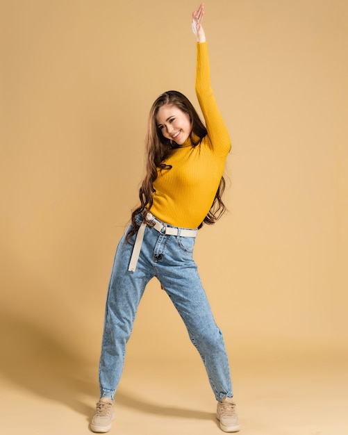 Jeune fille aux longs cheveux bouclés dans un sweat-shirt orange dansant avec sa main levée sur une orange pastel.