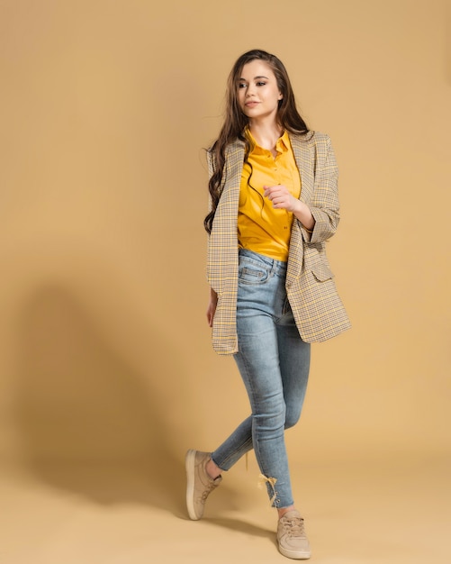 Photo jeune fille aux longs cheveux flottants dans une veste et une chemise jaune sur une orange pastel.