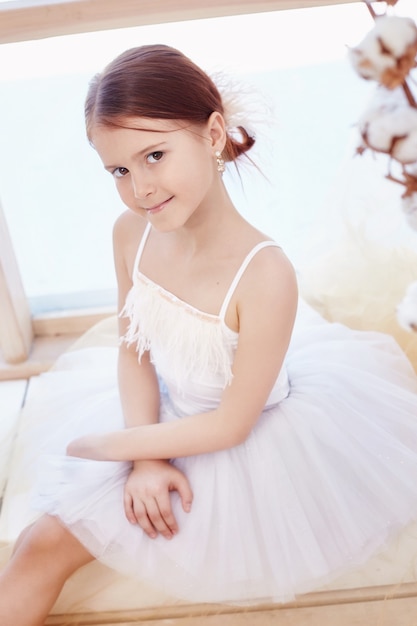 Jeune fille de ballerine se prépare pour une performance de ballet. Petit ballet prima. Fille dans une robe de bal blanche et Pointe près de la fenêtre, beaux cheveux roux