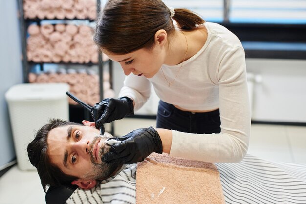 Une jeune fille Barber se rase la barbe, l'homme dans le salon de coiffure