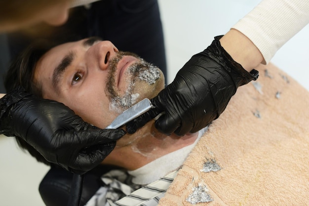 Une jeune fille Barber se rase la barbe, l'homme dans le salon de coiffure