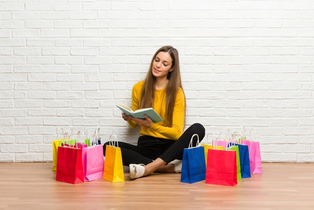 Jeune fille avec beaucoup de sacs à provisions tenant un livre et lire