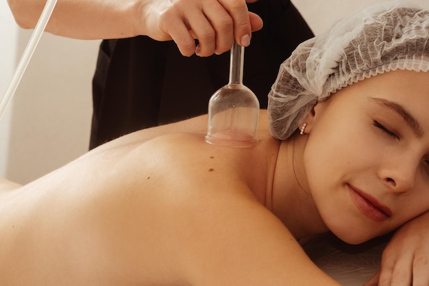 Une jeune fille belle allongée sur un canapé dans un chapeau cosmétique avec les yeux fermés dans un salon de spa masseur fait des procédures de massage