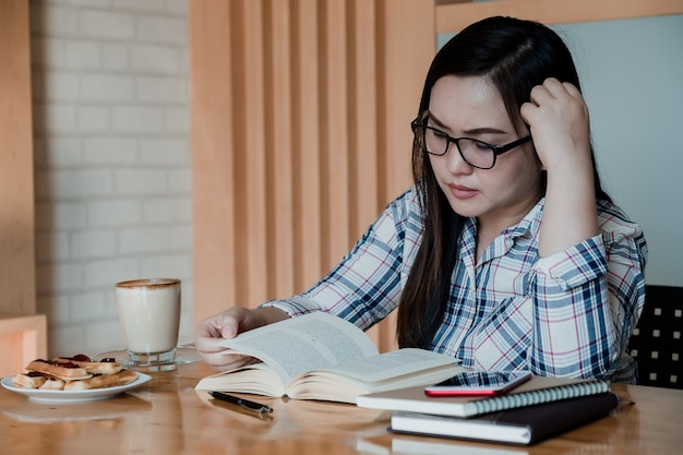 Photo jeune fille belle, assis par une table en bois et un livre de lecture.