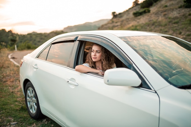 Photo jeune fille belle bouclée conduisant une voiture blanche à l'extérieur