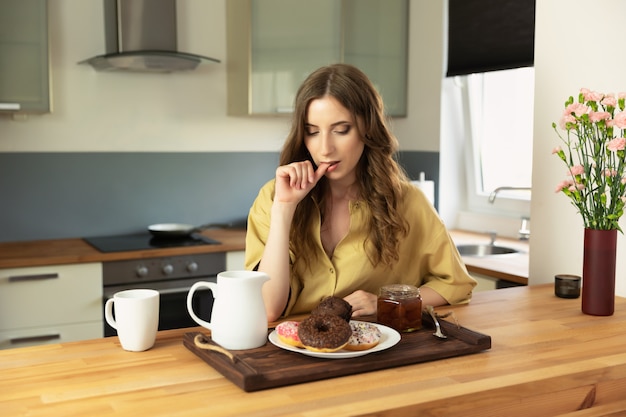 Jeune fille belle, prenant son petit déjeuner à la maison dans la cuisine. La fille mange des aliments malsains et riches en calories.