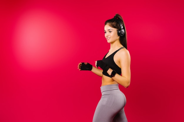 Une jeune fille avec une belle silhouette et en tenue de sport avec de gros écouteurs sur fond rouge