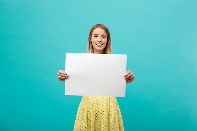 Jeune fille belle souriante et tenant une feuille de papier vierge, vêtue de jaune