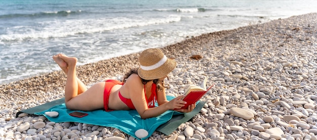 Une jeune fille en bikini lisant un livre sur la plage.