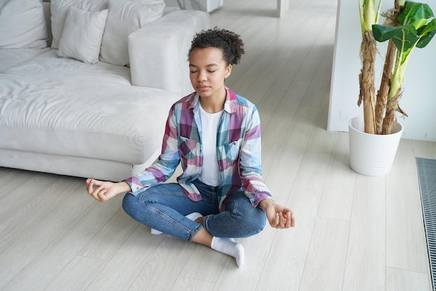 Jeune fille biracial pratiquer le yoga méditer faire des exercices de respiration à la maison bien-être de soulagement du stress