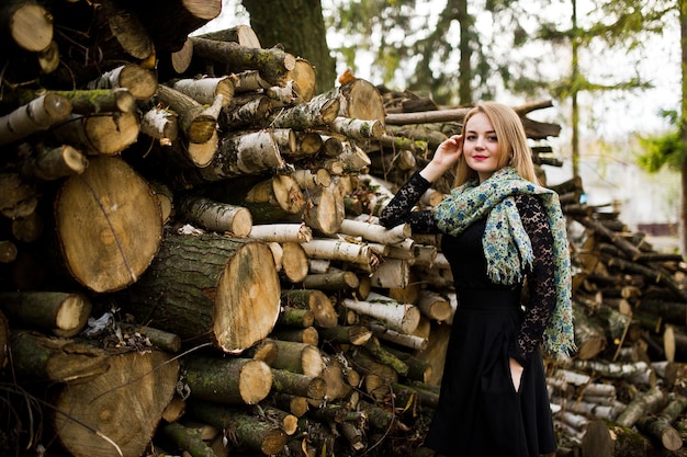 Jeune fille blonde au noir avec foulard posé sur fond de souches de bois