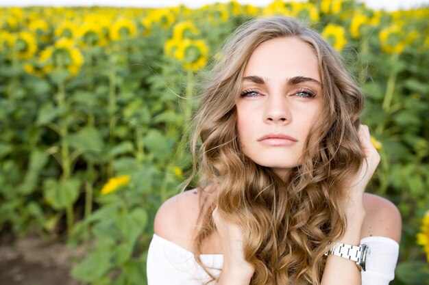 Une jeune fille blonde aux longs cheveux bouclés dans un champ de tournesols