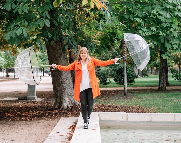 Jeune fille blonde aux yeux bleus et vêtue de soldes de gabardine rouge avec deux parapluies transparents dans un parc à Madrid Espagne