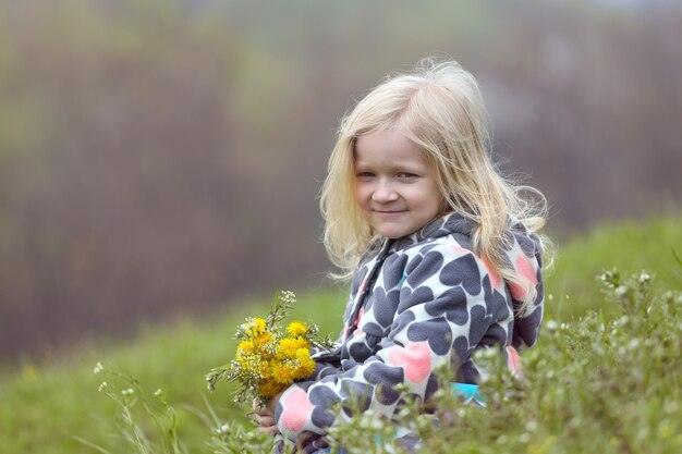 Jeune fille blonde avec bouquet de pissenlits sur une pelouse verte