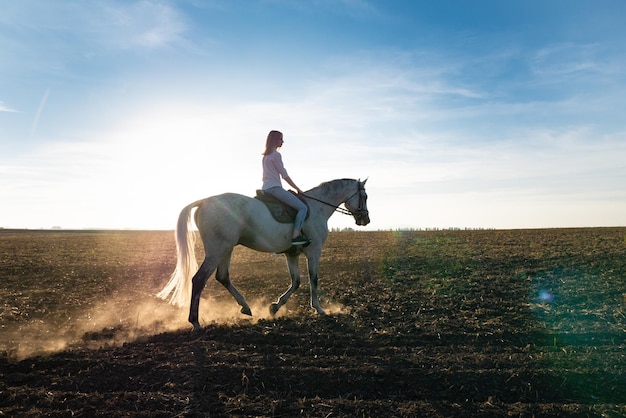 Jeune fille blonde à cheval sur le terrain pendant le coucher du soleil