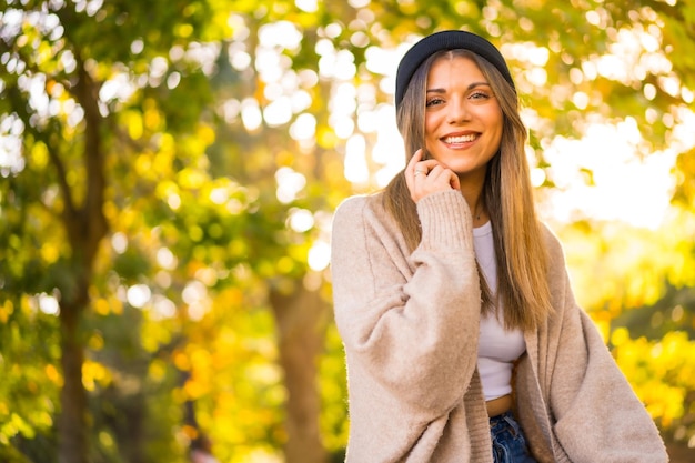 Une jeune fille blonde dans un chapeau de laine en automne assis dans le parc au coucher du soleil en souriant