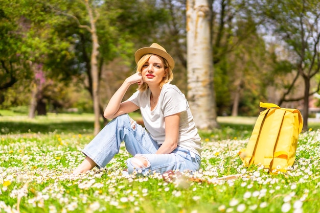 Une jeune fille blonde dans un chapeau profitant du printemps dans un parc en vacances en ville à côté de la nature et à côté des marguerites