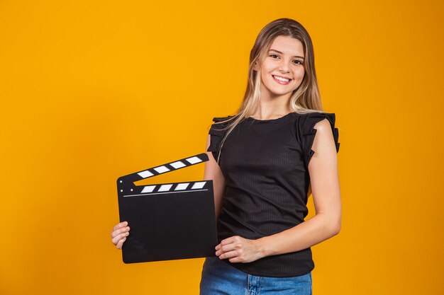 Jeune fille blonde dans des vêtements décontractés posant isolé sur fond de mur blanc portrait en studio. Concept de mode de vie des émotions sincères des gens. Simuler l'espace de copie. tenir un clap de cinéma.