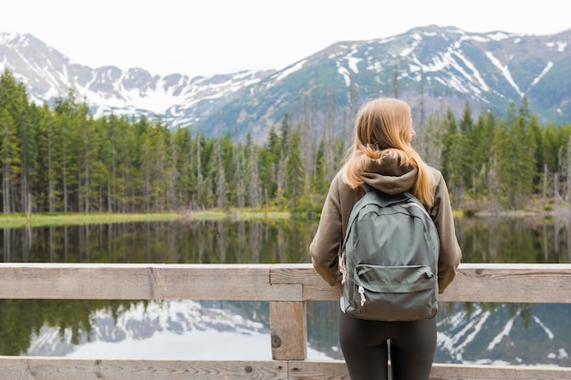 Jeune fille blonde debout au bord du lac de montagne dans les bois. Concept de voyage et de vie active. En plein air