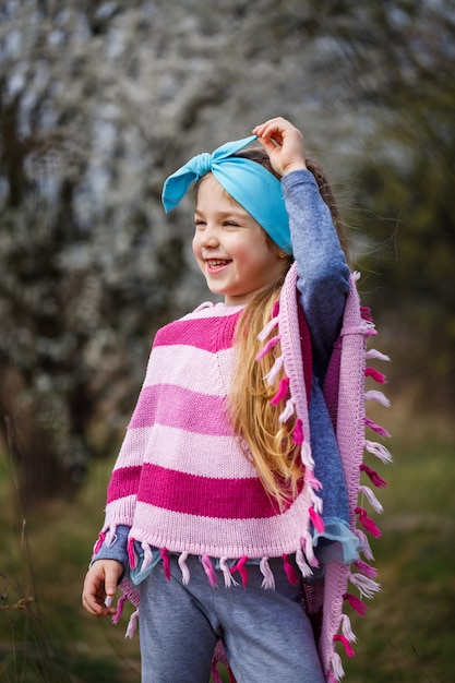 Jeune fille blonde debout dans un jardin fleuri. Cerisier en fleurs. Portrait de belle petite fille. Gros plan du petit visage du modèle. Floraison de Sakura, soirée de printemps