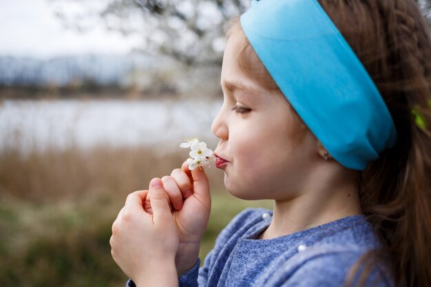 Jeune fille blonde debout dans un jardin fleuri. Cerisier en fleurs. Portrait de belle petite fille. Gros plan du petit visage du modèle. Floraison de Sakura, soirée de printemps