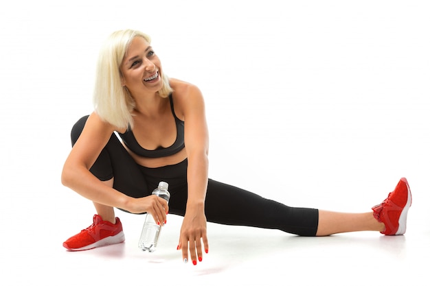 Jeune fille blonde fait du sport avec un uniforme de sport noir avec une bouteille d'eau