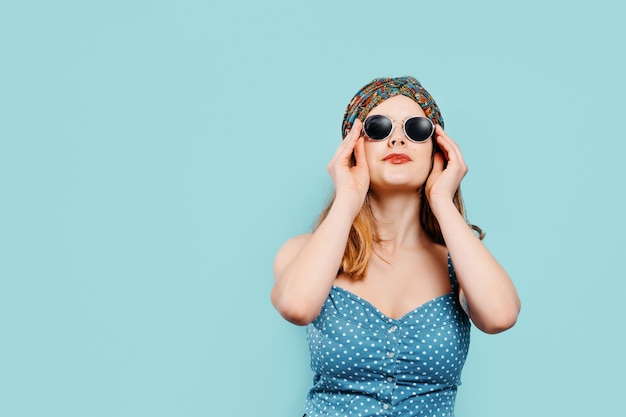 Jeune fille blonde avec un foulard lumineux portant des lunettes de soleil sur fond bleu