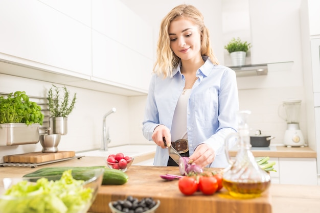 Jeune fille blonde heureuse préparant une salade saine dans la cuisine à domicile.