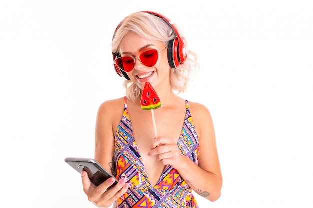 jeune fille blonde en maillot de bain et lunettes de soleil avec une sucette et un téléphone dans ses mains sur un matelas de natation