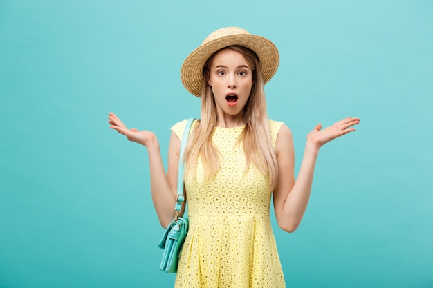 Jeune fille blonde mince avec de longs cheveux dans un chapeau se dresse et a ouvert sa bouche de surprise.