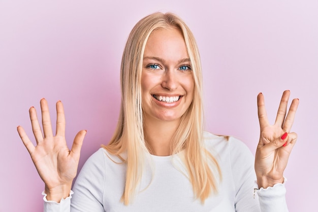 Jeune fille blonde portant des vêtements décontractés montrant et pointant vers le haut avec les doigts numéro huit tout en souriant confiant et heureux.