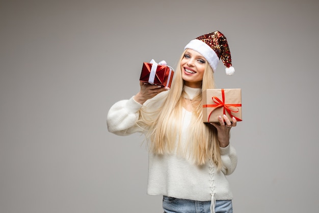 Jeune fille blonde de race blanche en bonnet de Noel étincelant holdig deux cadeaux