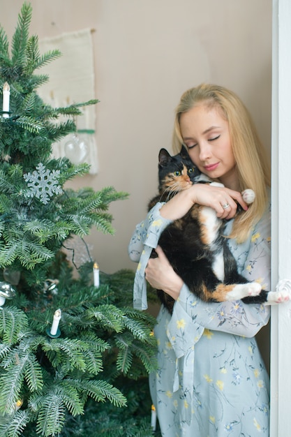 Jeune Fille Blonde En Robe élégante Tenant Un Chaton Drôle Dans La Chambre Avec L'arbre De Noël