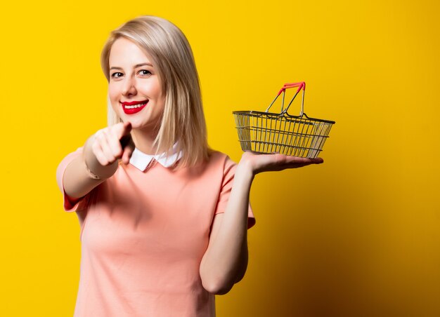 Photo jeune fille blonde en robe rose avec panier sur espace jaune