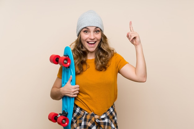 Jeune fille blonde skateur sur mur isolé pointant vers le haut une excellente idée