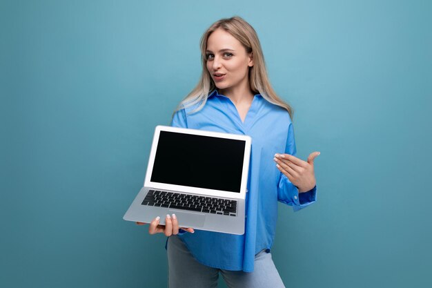 Jeune fille blonde souriante avec un ordinateur portable dans ses mains avec un espace vide pour une page web sur un bleu