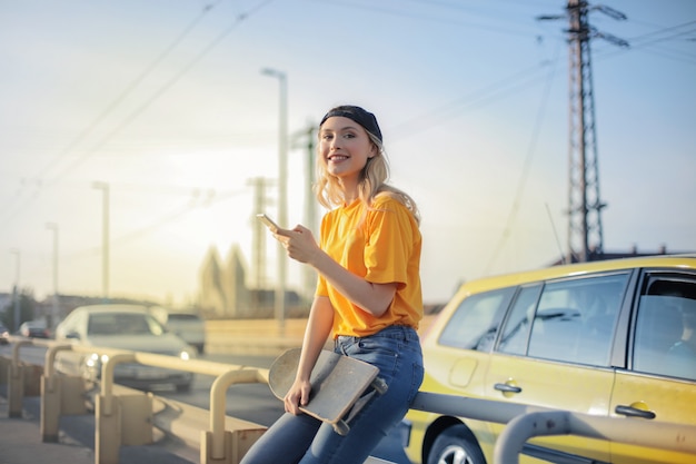 Jeune fille blonde souriante avec un skateboard dans la ville