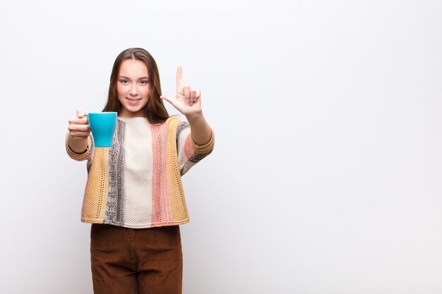 Jeune fille blonde avec une tasse de café contre le mur blanc