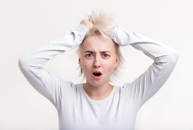 Photo jeune fille blonde tenant ses cheveux sur un fond blanc émotion lumineuse en état de choc