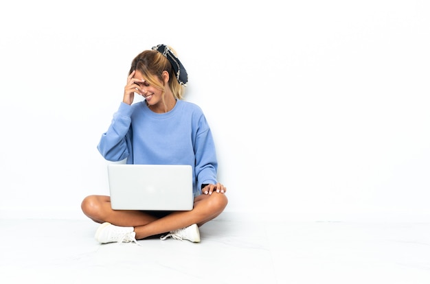 Jeune fille blonde uruguayenne avec l'ordinateur portable isolé sur un mur blanc en riant