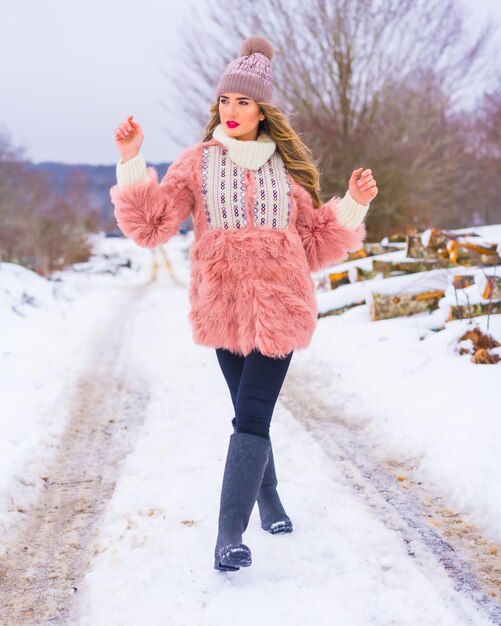 Jeune fille blonde en veste de fourrure rose bottes d'hiver et un chapeau violet dans la neige