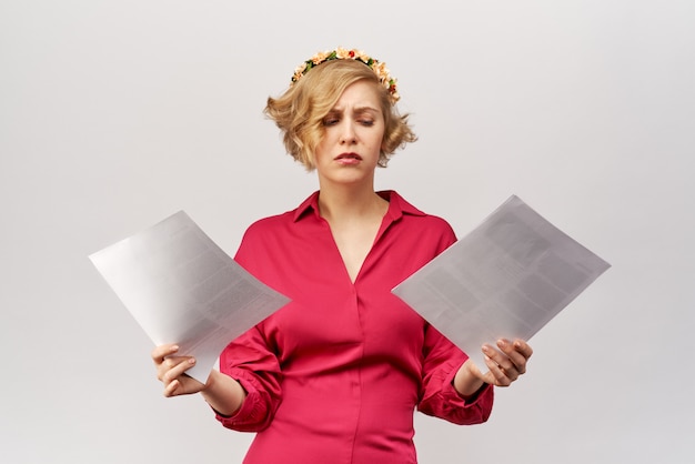 Une jeune fille blonde avec une vue perdue regarde les documents étalant ses mains devant elle dans la confusion et l'incompréhension.