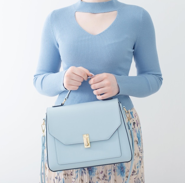 Jeune fille en blouse bleue et jupe plissée avec sac à main bleu sur fond blanc