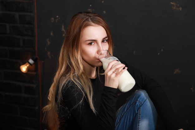 La jeune fille boit du lait d'une bouteille sur un fond de mur noir