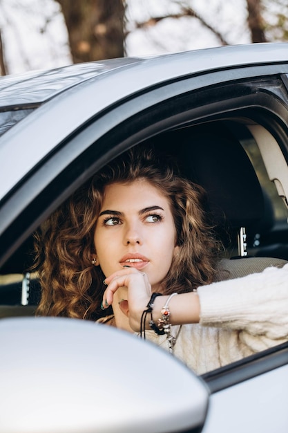 Photo une jeune fille bouclée dans un pull blanc sur le fond de la nature d'automne et de sa propre voiture